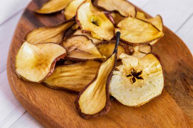 Ahşap bir tahtanın üzerinde kurumuş armut ve elma dilimlerini, dokuları ve doğal tonları renklendiren detaylı bir görünüm.