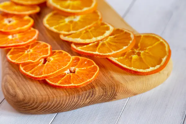 Ahşap bir tahtanın üzerinde kurumuş portakal dilimlerine odaklanan detaylı manzara narenciye deseni ve parlak rengi yakalıyor.