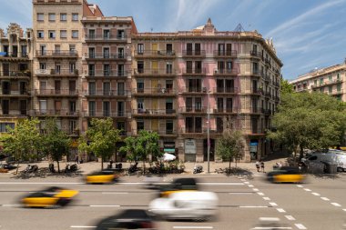 Barselona, İspanya - 13 Temmuz 2024. Süslü balkonlarla simetrik cephe ve Eixample mahallesinde geniş bir caddede trafiği hareket ettirme