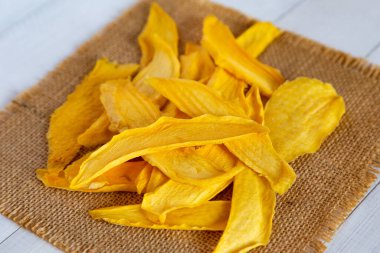 Beyaz ahşap yüzeyde desenli bir çuval bezi kareye yerleştirilmiş altın kurutulmuş mango dilimlerinin ayrıntılı görüntüsü