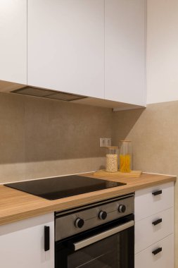 Pürüzsüz modern bir tasarımla mutfak ocağı, fırın, ahşap tezgah ve beyaz dolapların detaylı yakın çekimi