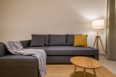 Oturma odasının köşesinde yumuşak battaniyeyi yan taraftaki ahşap masa ve lambayla gösterirken.