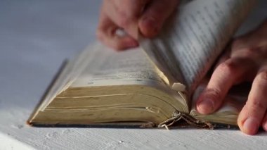 Yıpranmış, yıpranmış kenarlarını ve eski kağıt dokusunu gözler önüne seren eski bir kitaptan sayfalar çıkaran ellerin yakın çekimi..