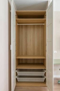 Açık beyaz kapıları olan boş bir ahşap gardırop rafları ortaya çıkarıyor. Bir asma çubuk ve en altta iki ağ depolama sepetleri..