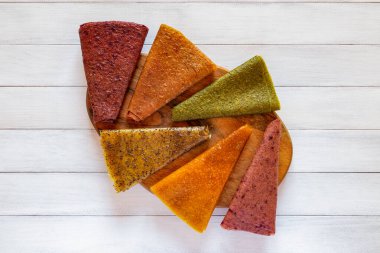 Görsel çeşitlilik için ahşap bir tahtanın radyal düzeninde sergilenen üç köşeli meyve pastil parçalarının renkli bir karışımı