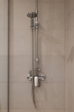 Krom armatür ve el yapımı duş başlığı nötr fayanslı duvara monte edilmiş modern bir duş düzeneği.