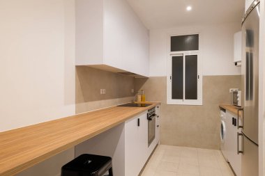 Yan taraftaki mutfak manzarasında beyaz dolaplar, ahşap tezgah ve parlak ocak ve fırın görünüyor.