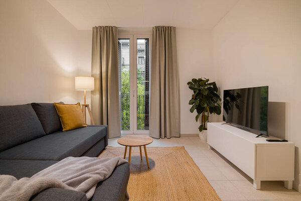 Neutral tone living room with gray sectional sofa, TV, indoor plant and bright balcony window space