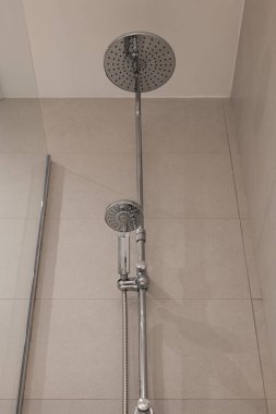 Kapalı bir krom duş armatürü. Yuvarlak başlığını ve el yapımı duş başlıklarını banyoda gösteriyor.