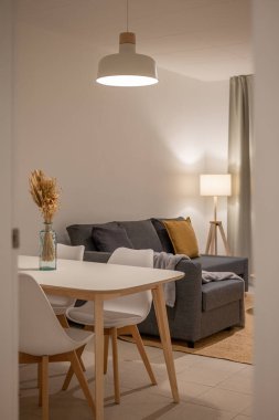 Kurumuş çiçekler, beyaz sandalyeler ve arka planda gri kanepe olan bir yemek masası.