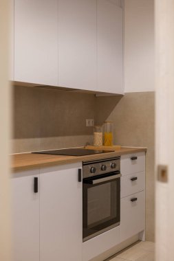 Temiz beyaz dolabı olan parlak bir mutfak, ahşap atölye, elektrikli hob ve makarna ve tahıllı kavanozlar.