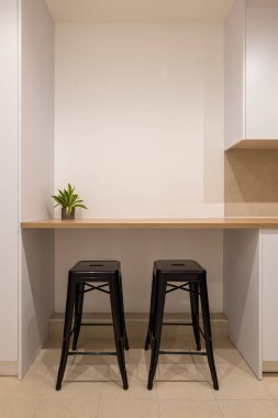 Basit mutfak alanı, ahşap tezgah barı, siyah tabure ve beyaz dolaplar.