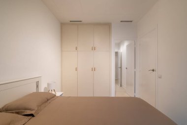 Yatak odasının içi boz yatak odası ve minimalist, nötr tonlu bir tasarımla döşenmiş gardırop.