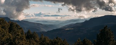 Yoğun bulutların altındaki uzak dağların geniş görüşü sisi delip geçen ışık huzmeleriyle