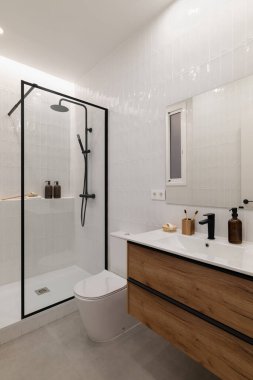Cam duşlu modern banyo, ahşap kibir ve minimalist dekor. Tarafsız renkler temiz ve ferah bir atmosfer yaratır