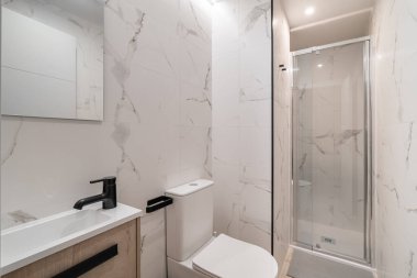 Mermer duvarlı modern banyo, cam duş ve parlak bir lavabo. Tasarım, nötr renkler ve temiz çizgilerle minimalist ve çağdaş.