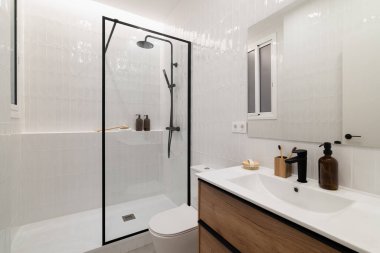 Cam duşlu modern banyo, beyaz fayanslar, ahşap kibir ve minimalist dekor. Çağdaş yaşam alanları için temiz ve şık tasarım.
