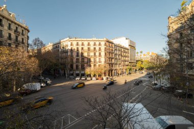 Barselona 'da sarı taksiler, binalar ve açık mavi gökyüzü olan bir şehir manzarası. En az trafiği olan yoğun bir kavşağın gündüz görünümü.