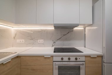 Beyaz dolaplı modern mutfak, mermer kaplama ve paslanmaz çelik aletler. Parlak ışıklandırmalı temiz ve minimalist tasarım.