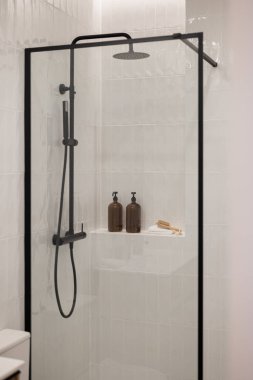 Cam kaplamalı modern duş, siyah eşyalar ve minimalist tasarım. Raftaki iki kahverengi şişe biraz zarafet katar.