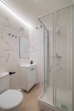Cam banyosu, beyaz tuvaleti ve gösterişli gösterişi olan modern bir banyo. Mermer duvarlar temiz ve zarif bir atmosfer yaratır.