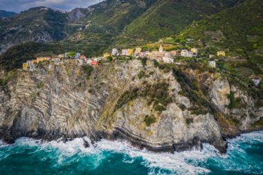 İtalya, Liguria, Cinque Terre, Corniglia, tepeler arasında çok renkli kasaba mimarisi. Deniz kenarından insansız hava aracı görüntüsü. Eylül 2022