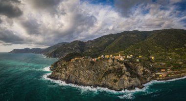 İtalya, Liguria, Cinque Terre, Corniglia, tepeler arasında çok renkli kasaba mimarisi. Deniz kenarından hava aracı panoramik görüntüsü. Eylül 2022