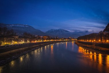 İtalya 'nın Trento kentinin arka planında karlı dağ manzarası. Dağlar ve Adige nehri arasındaki bir şehrin gece manzarası. Ocak 2023 'te uzun pozlama fotoğrafı çekildi.