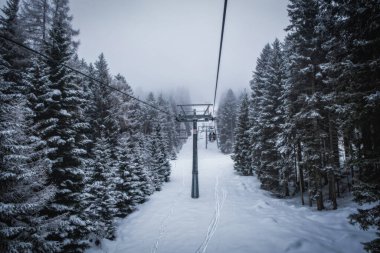 Karlı dağda sisli bir günde kayakçılar ve snowboardcular kayak kaldırıyor. Donmuş füniküler. Pinzolo ve Madonna di Campiglio kayak merkezi. Ocak 2023