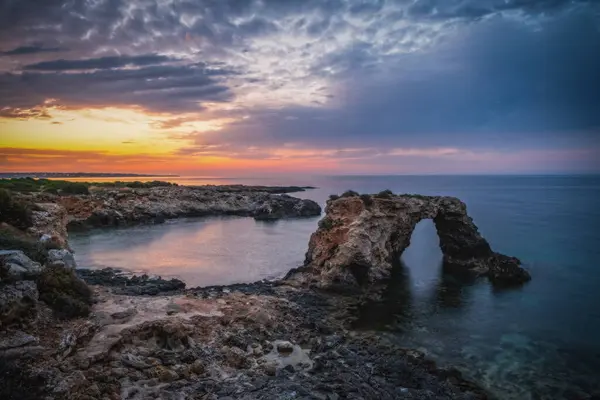 stock image Rocky coastline with a natural arch at punta Asparano, near Siracusa. Sunrise time. June 2023