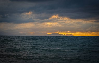 Güzel dağları ve güzel seyahat manzarasının arka planında inanılmaz bulutlu gökyüzü olan günbatımı deniz körfezi manzarası. Sicilya, Campofelice di Roccella. Ağustos 2024