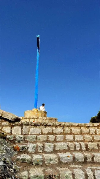 A person prays at the foot of a blue wooden cross on the hill.