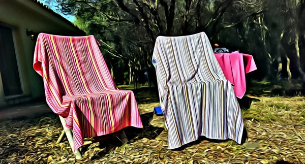 Beach towels hung out to dry in the sun on the deck chairs in the garden during the summer.