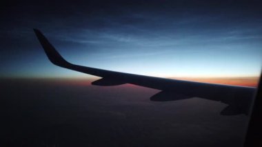 Gün batımında bulutların üzerinde uçan bir uçağın silüeti..