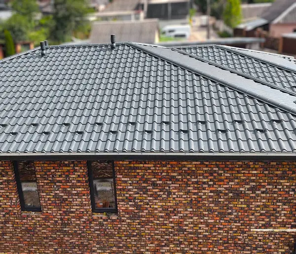 Çelik çatı kaplaması olan kapalı bir çatı. Geleneksel metal kiremitler. Gri modüler fayans efekti çatı paneli. Çamur ya da beton levha olarak metalik kıvrımlı külotlar. Bina kapatıyor.