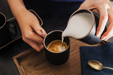 Female hands pouring  milk foam into espresso , Preparing, making cappuccino.