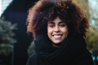 Portrait beautiful young dark-skinned woman. African american ethnicity female with black curly hair showing white teeth outside in casual clothes