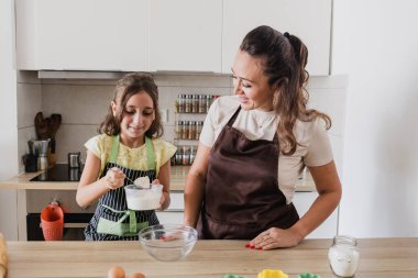 Önlüklü anne ve çocuk birlikte kek pişiriyorlar.