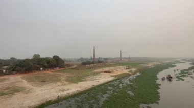 Nehir kenarında küçük bir nehir ve tuğla ocağı olan kırsal bir bölgenin manzarası. Kanalda küçük su damarları olan güzel bir doğa manzarası. Nehir kıyısında oynayan çocuklar ve nehirde hareket eden tekneler.