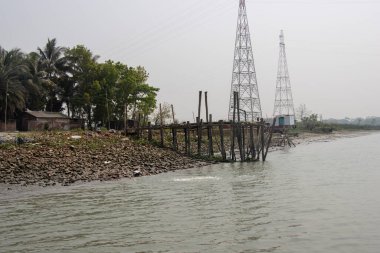 Kırsal bölge trol teknesi ve güzel bir nehri olan tekne iskelesi. Nehir kıyısı manzaralı, büyük elektrik direkleriyle ve mavi gökyüzüyle. Nehir kıyısı ve tekne rıhtımı olan güzel bir doğa manzarası. Manzaralı köy bölgesi nehri.