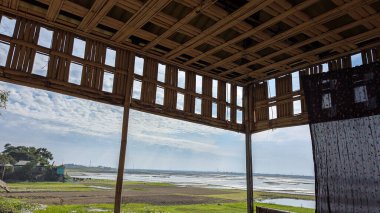 Open structure with bamboo walls overlooking a serene landscape of rice fields and a cloudy sky during the day clipart