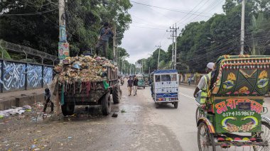 Şehir işçileri, yoğun bir caddede gündüz vakti yemyeşil ve yerel trafik ile çevrili çöpleri topluyor.