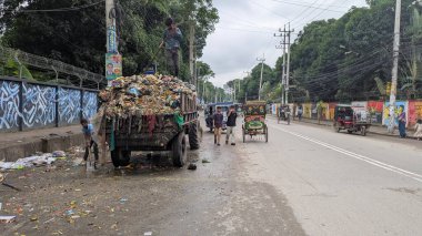 Kalabalık bir çöp kamyonunun yanında çalışan insanlar kalabalık bir şehir caddesinde ağaçlar ve renkli duvar resimleri olan bulutlu bir günde