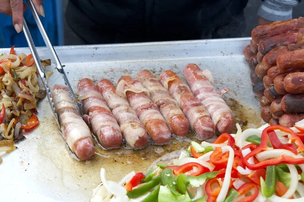 Straatverkoper Bakt Spek Gewikkelde Hotdogs Tang Verandert Voedsel Populaire Keuken Rechtenvrije Stockafbeeldingen