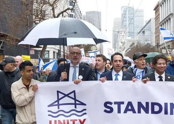 San Francisco, CA - 03 Mart 2024: Politikacılar ve tanımlanamayan katılımcılar Pazar Caddesi 'ndeki Anti-Semitizm karşıtı bir yürüyüşe katıldılar. Yağmurda yürürken.