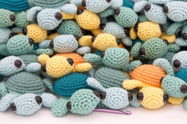 Bir sürü el yapımı, yeşil ve turkuaz örgü kaplumbağa, sarı ve turuncu örgü örme kancalı, soluk beyaz arka planda..