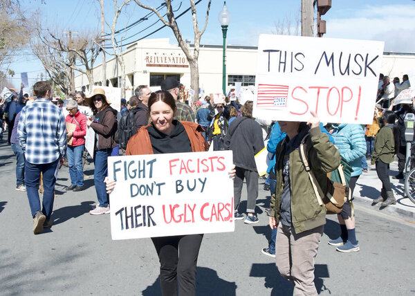 Berkeley, CA - March 1, 2025: Protestors hoding signs blocking traffic in front of a Tesla showroom. Denouncing Musk and calling for a boycott as a result of his recent actions on Capitol Hill.