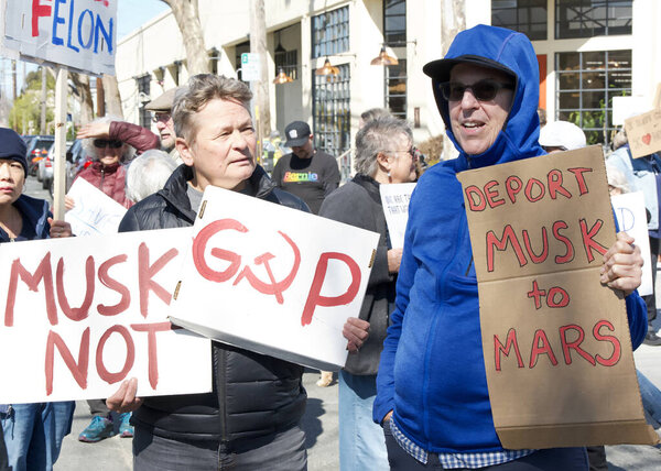 Berkeley, CA - March 1, 2025: Protestors hoding signs blocking traffic in front of a Tesla showroom. Denouncing Musk and calling for a boycott as a result of his recent actions on Capitol Hill.