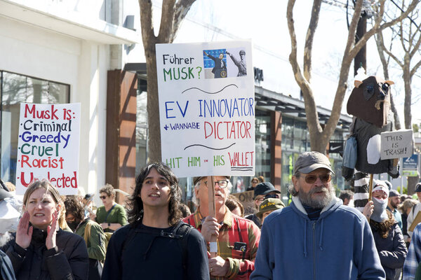Berkeley, CA - March 1, 2025: Protestors hoding signs blocking traffic in front of a Tesla showroom. Denouncing Musk and calling for a boycott as a result of his recent actions on Capitol Hill.
