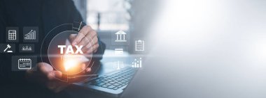 Adam akıllı telefonu elinde tutuyor ve baro vergisi olan bir dizüstü bilgisayar kullanıyor ve vergilendirme işletmelerinin vergi iadesi, ekran medyası, tablet bilgisayar ve vergi iadesi ile ilgili grafik ve grafikler ekranda gösteriliyor.